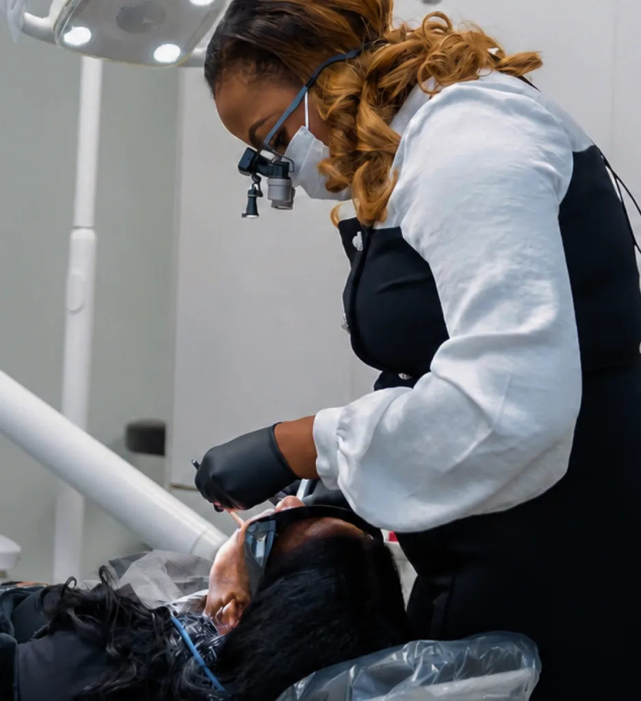 Dentist wearing magnification loupes and gloves examining a patient's teeth in treatment chair