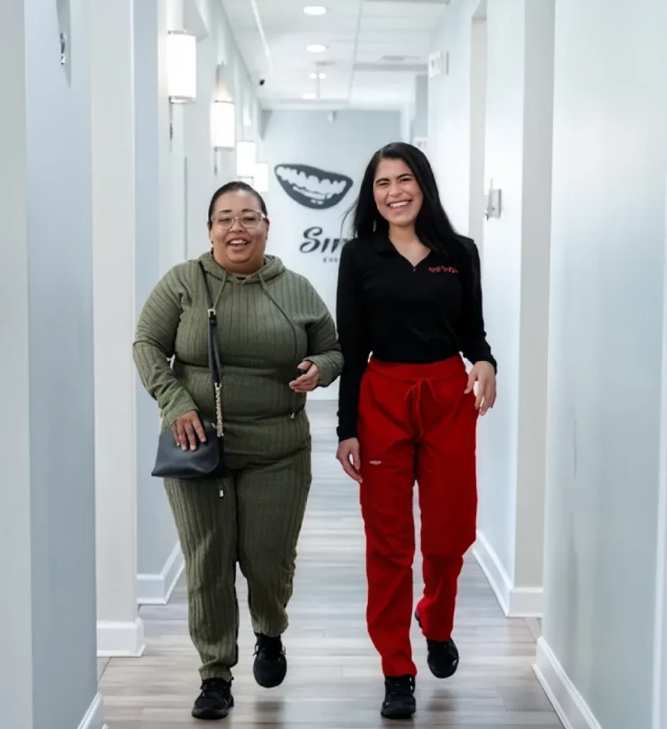 Two dental team members walking together down a bright hallway with smile graphic on wall