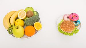 Two plates comparing healthy foods like fruits and vegetables on left with unhealthy burger and donut on right