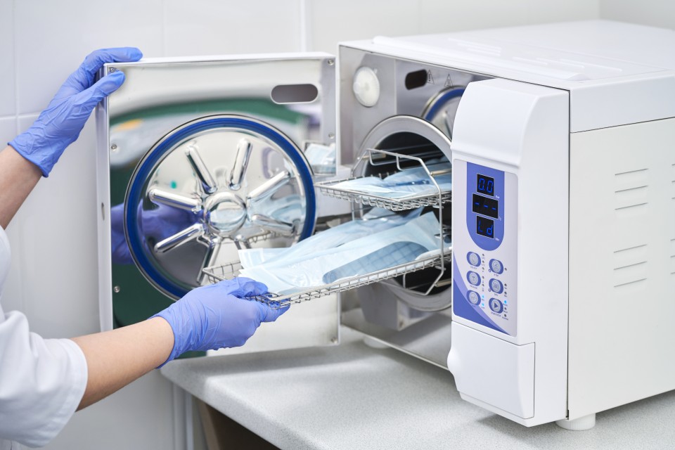 Dental staff member in blue gloves removing sterilized instruments from an autoclave sterilizer