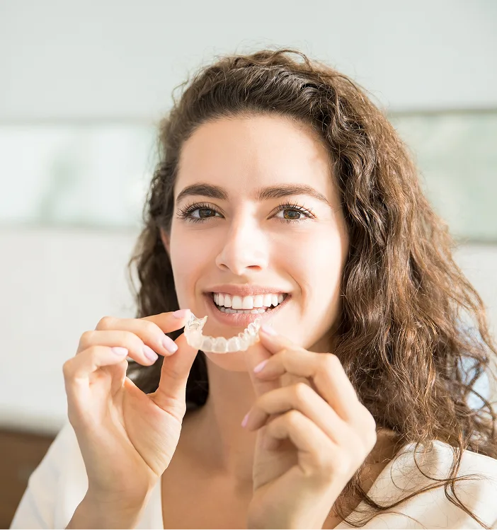 Woman holding a clear Invisalign aligner tray and smiling at the camera