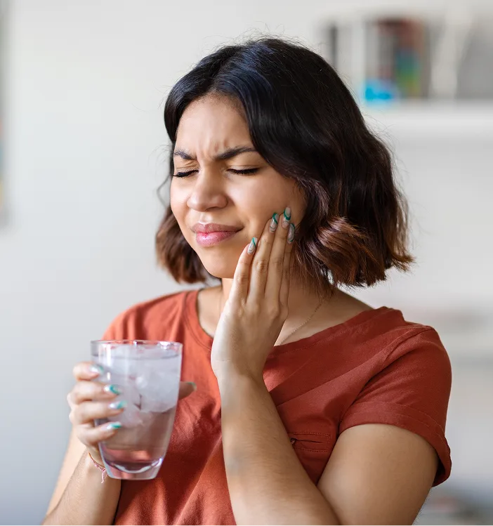 Woman holding glass of water and touching cheek in pain, suggesting tooth extraction discomfort
