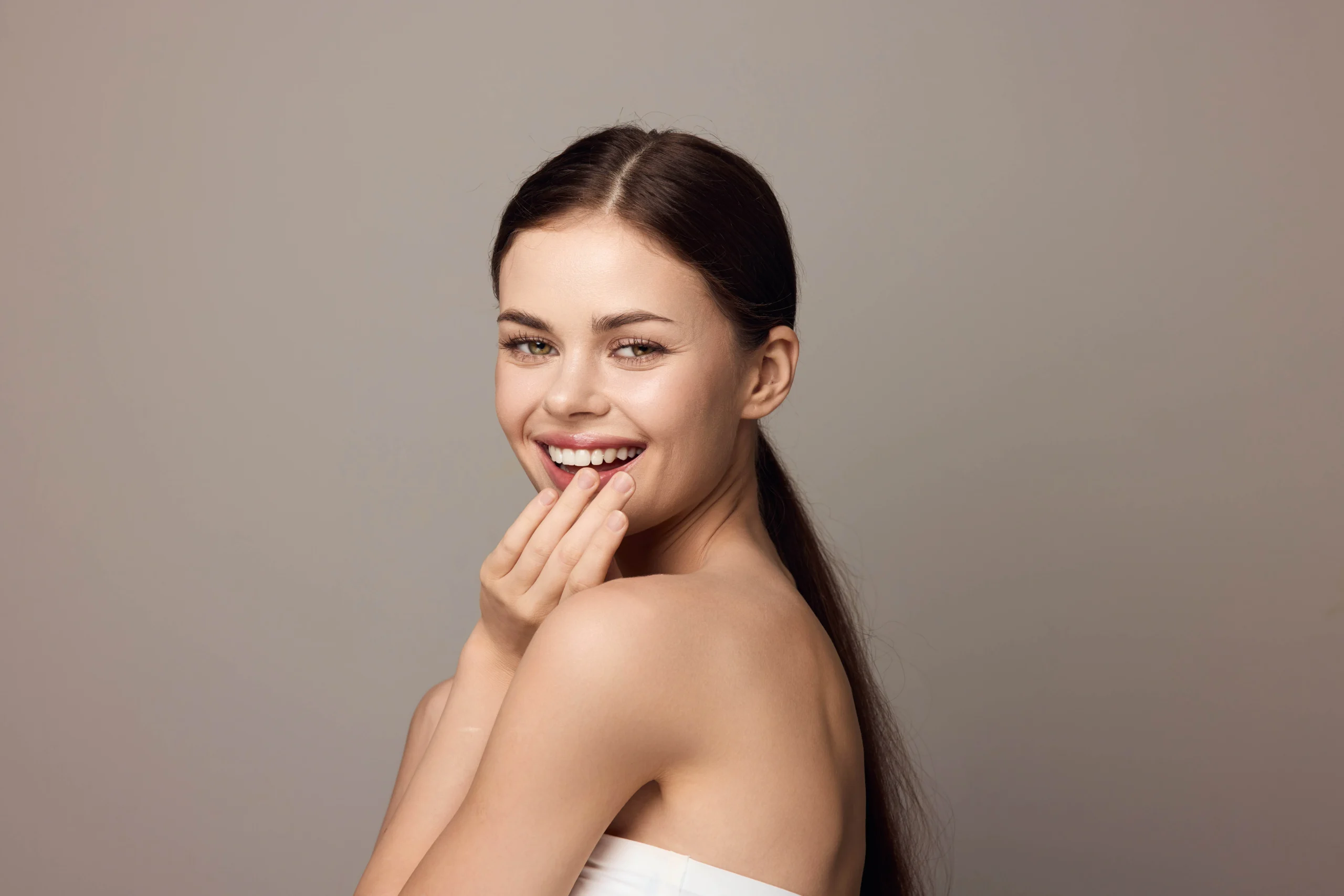 Young woman smiling with hand near her mouth against a gray background