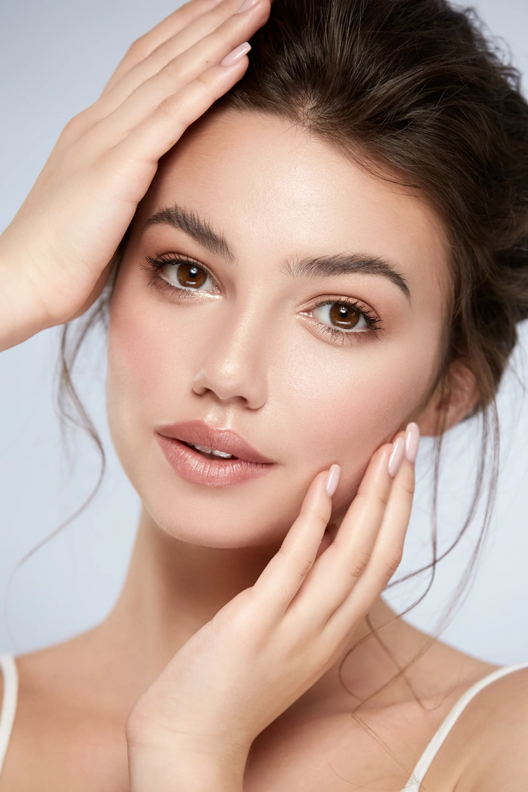 Woman with smooth, radiant skin touching her face against a neutral background