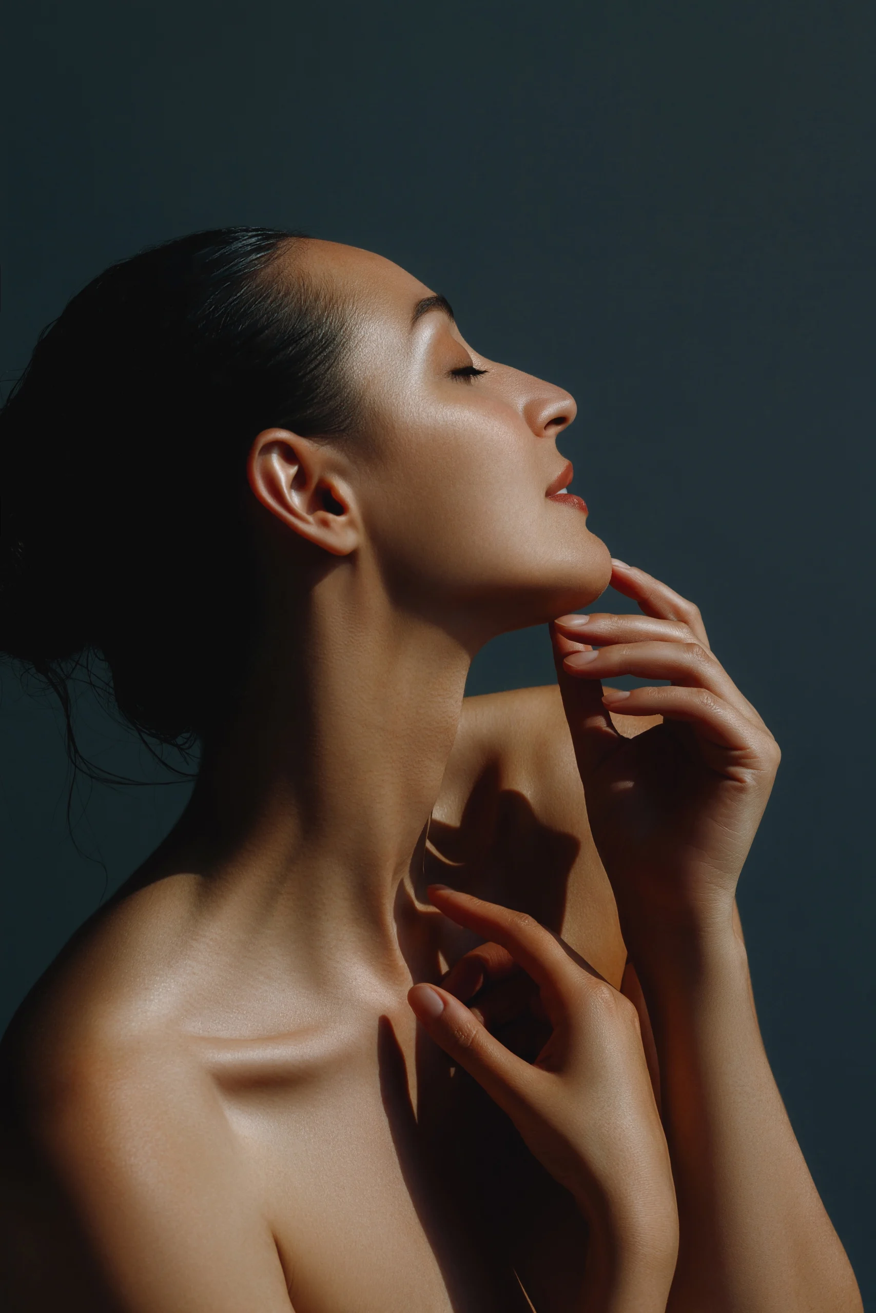 Woman in profile with smooth, glowing skin touching her chin and neck
