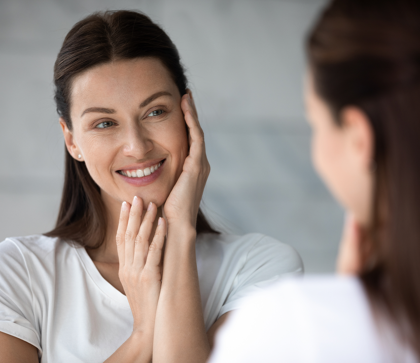 Woman smiling while touching her face during a virtual skincare consultation
