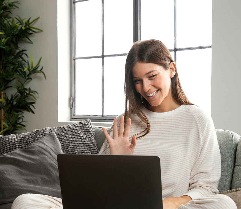Woman waving at laptop during a virtual visit consultation from home