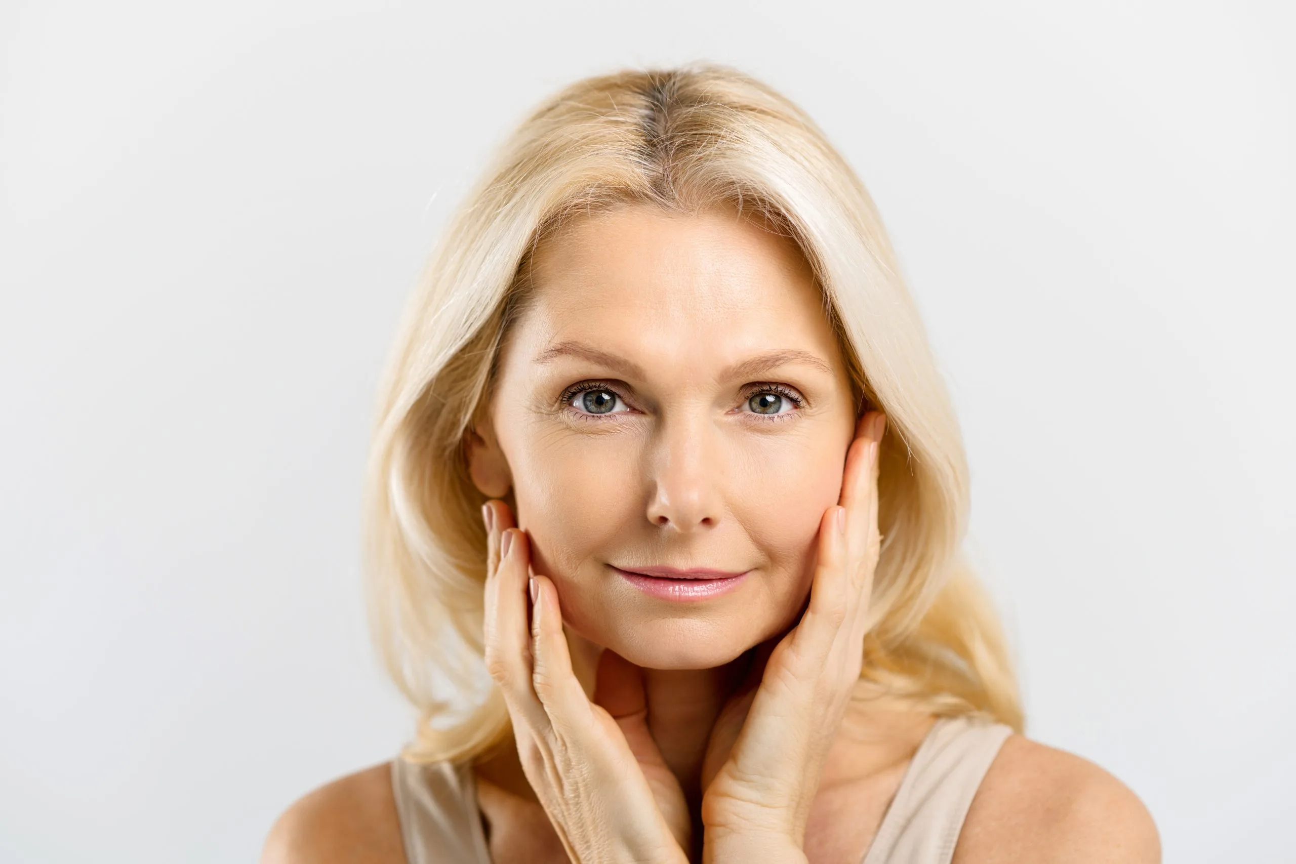 Mature blonde woman with hands framing face, smiling at camera