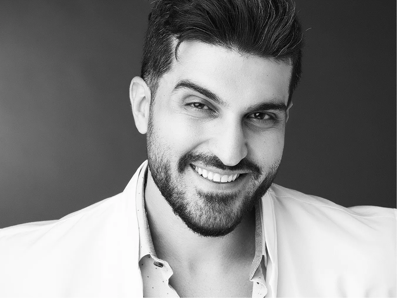 Man with dark hair and beard smiling at camera in white collared shirt