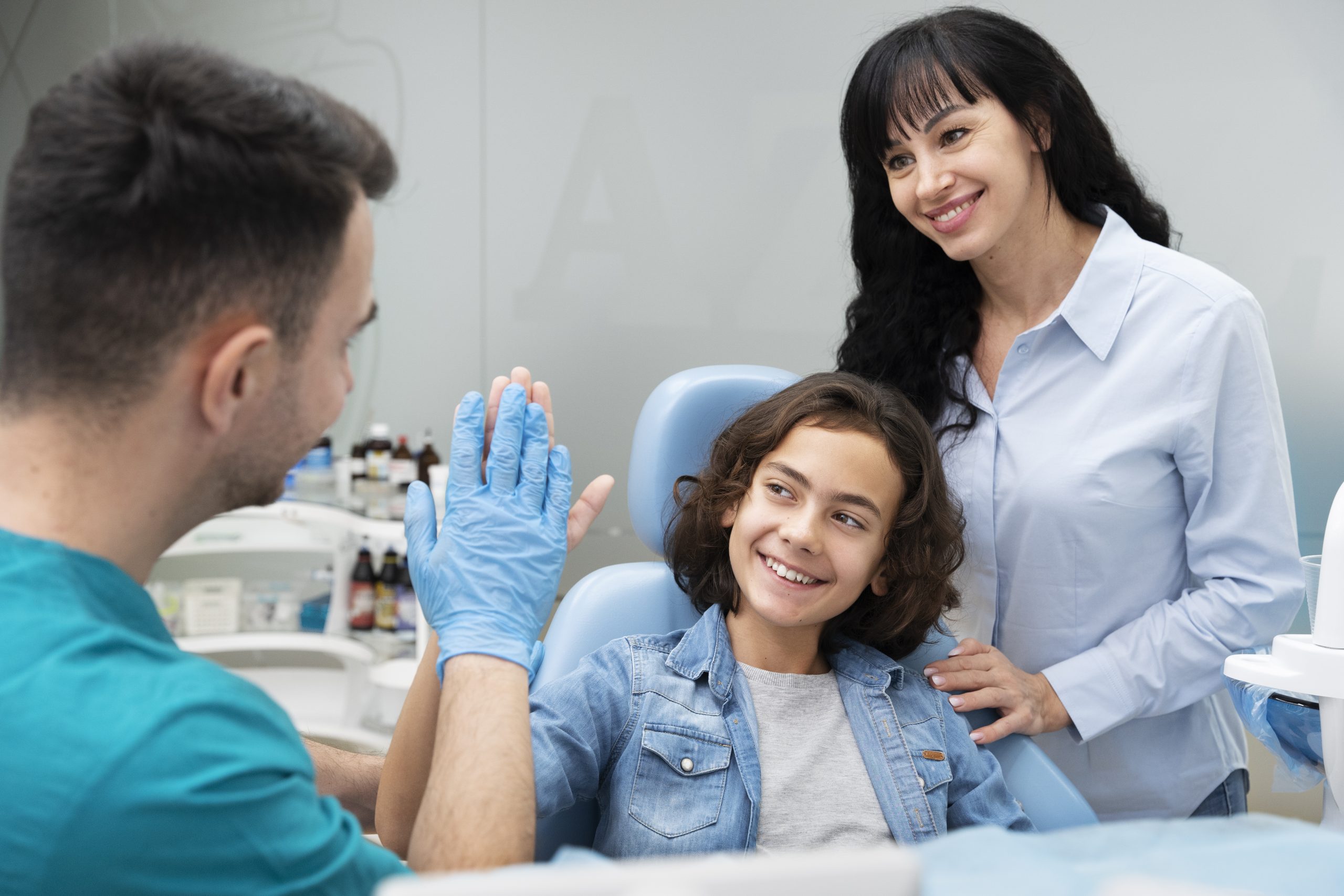 Dentist and assistant high-fiving young male patient in dental clinic treatment room
