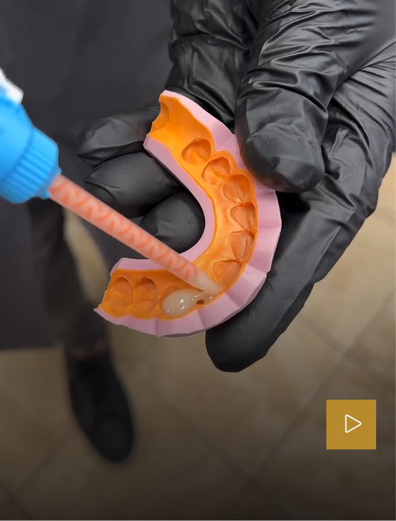 Hands holding pink and orange dental aligner model with blue instrument