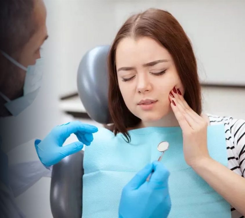 Patient in dental chair touching cheek in discomfort while dentist examines tooth