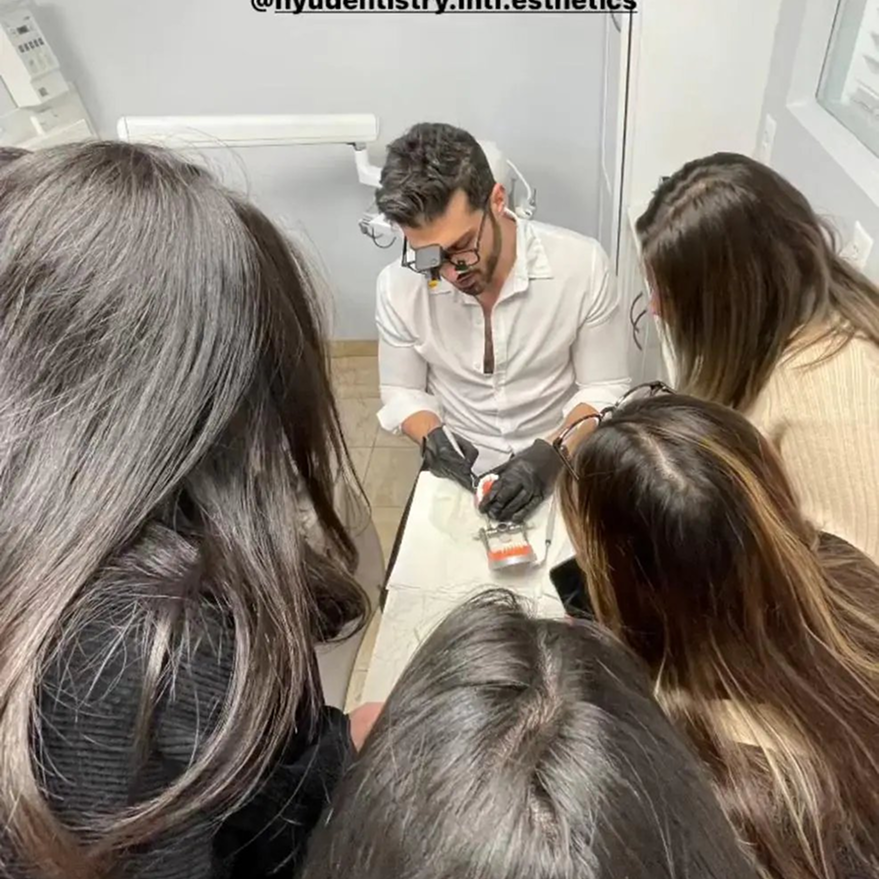 Dentist in white shirt and gloves demonstrating treatment to group of patients in clinical setting