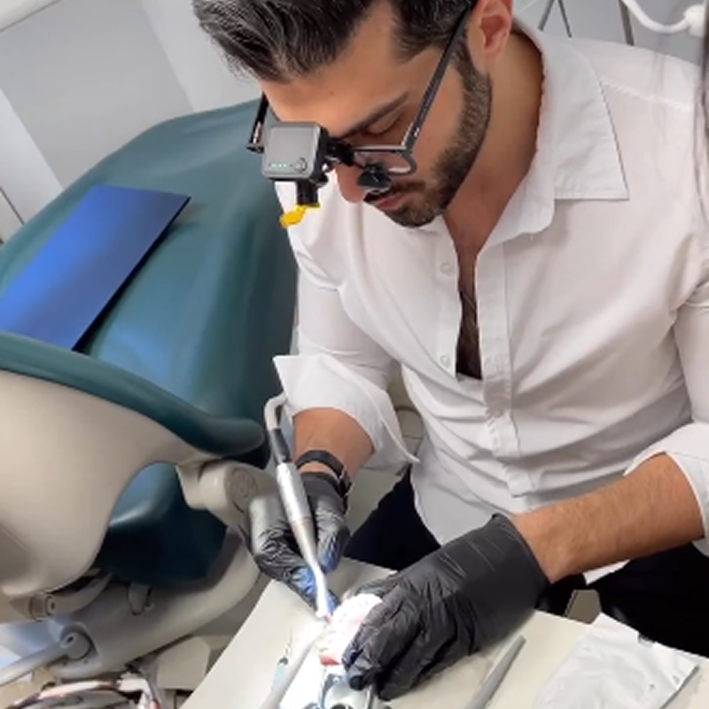 Dentist in white coat and magnification loupes performing chairside dental treatment on a patient