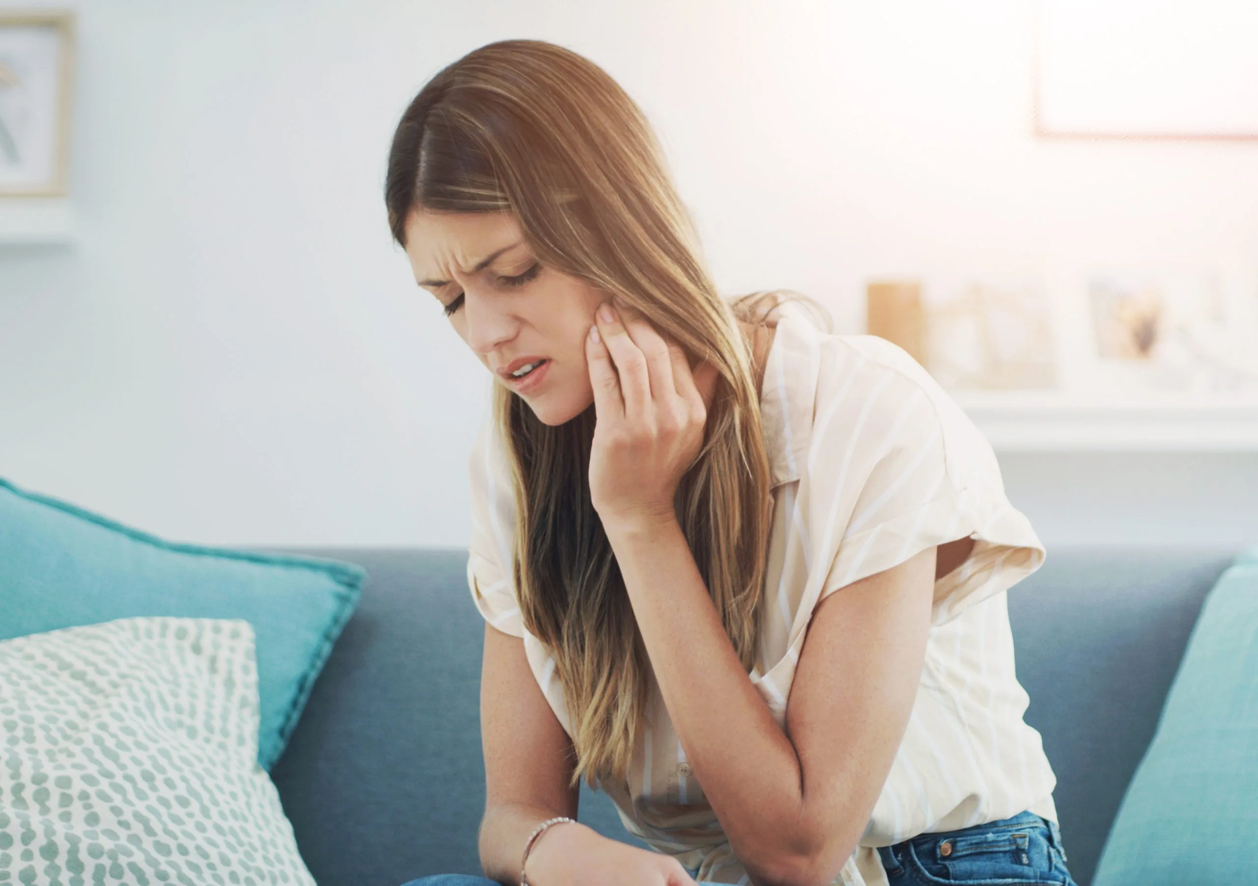 Woman sitting on a couch holding her jaw in discomfort from a painful mouth ulcer
