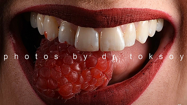 Person eating a raspberry while displaying a bright smile with natural teeth