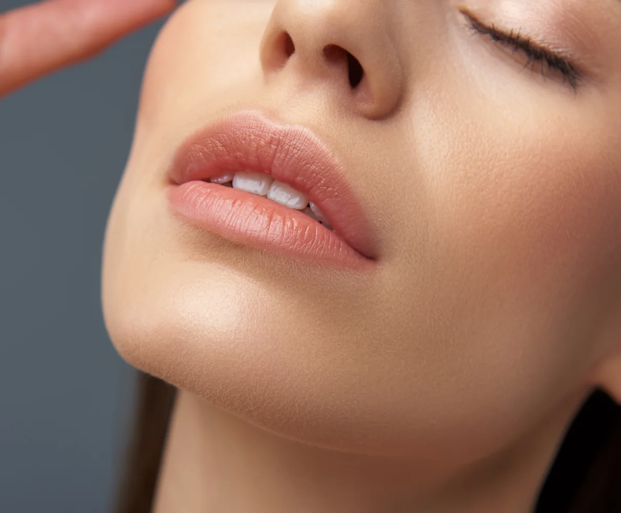 Close-up of person's lower face showing full lips and smooth skin against neutral background