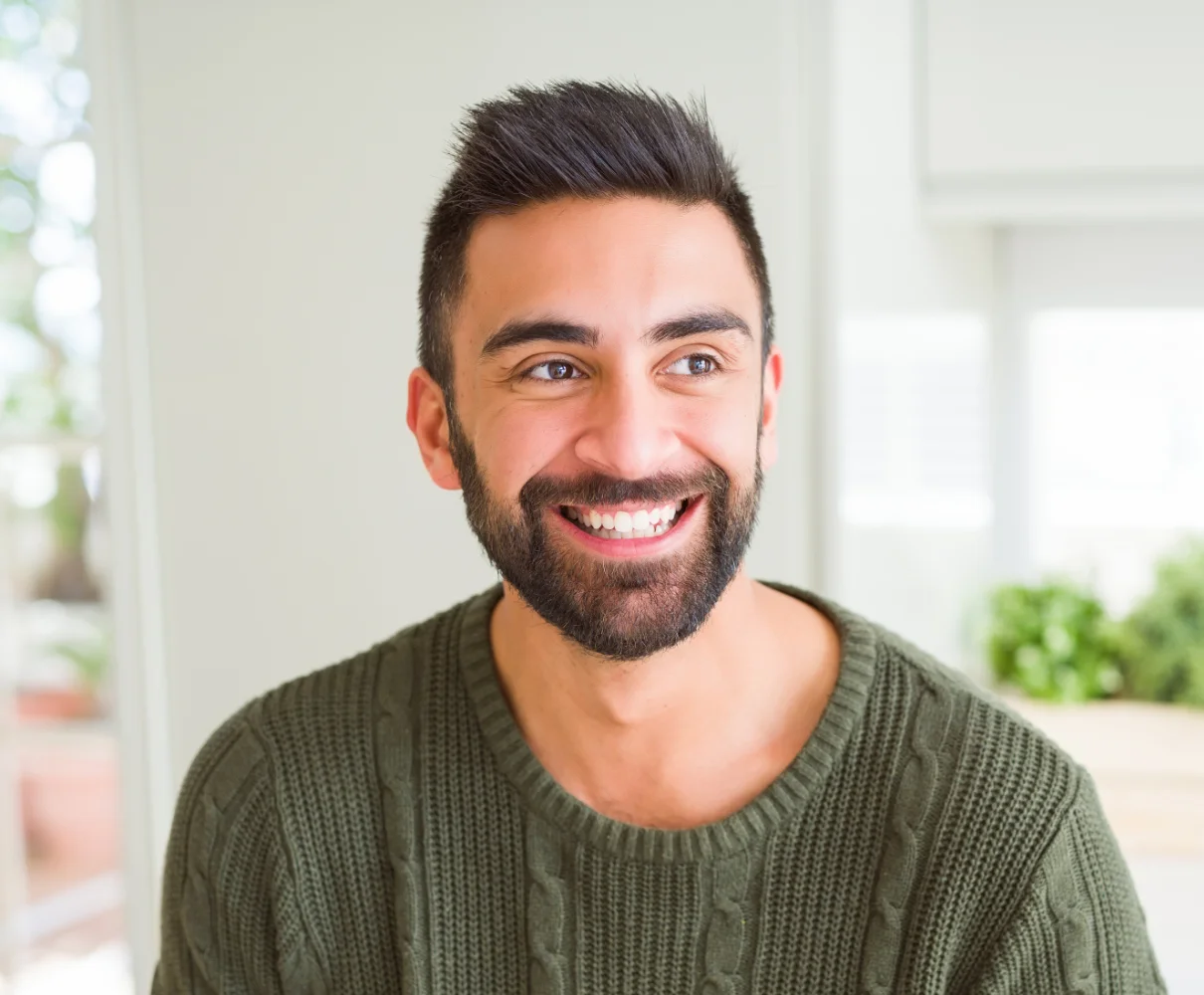 Man smiling at camera in bright interior space wearing olive green sweater