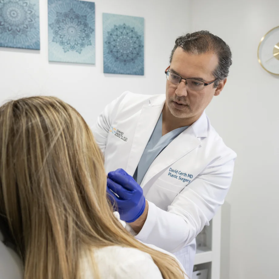 Plastic surgeon in white coat and blue gloves examining patient's face in clinical setting