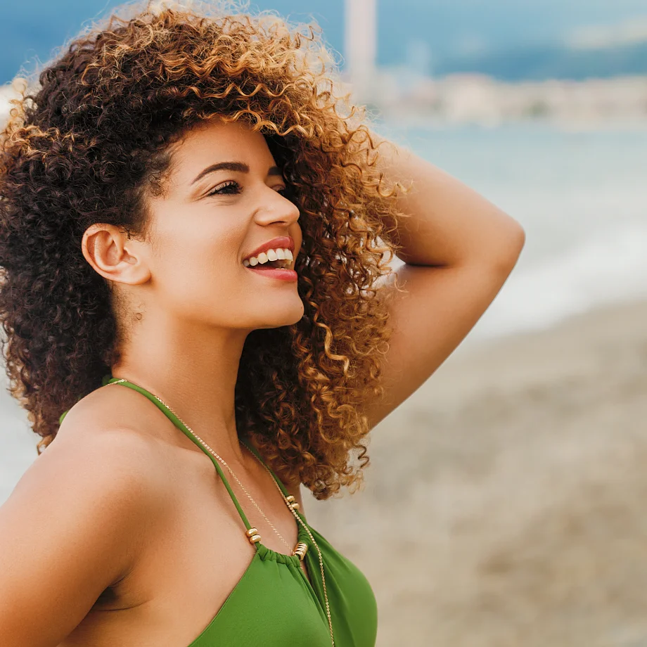 Woman with curly hair smiling in profile at a beach