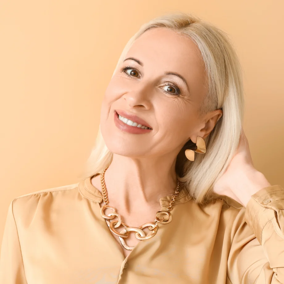 Mature woman with white hair smiling, wearing gold chain necklace and beige top