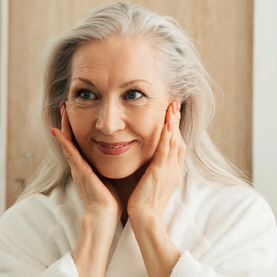 Mature woman with white hair smiling at camera, hands framing her face