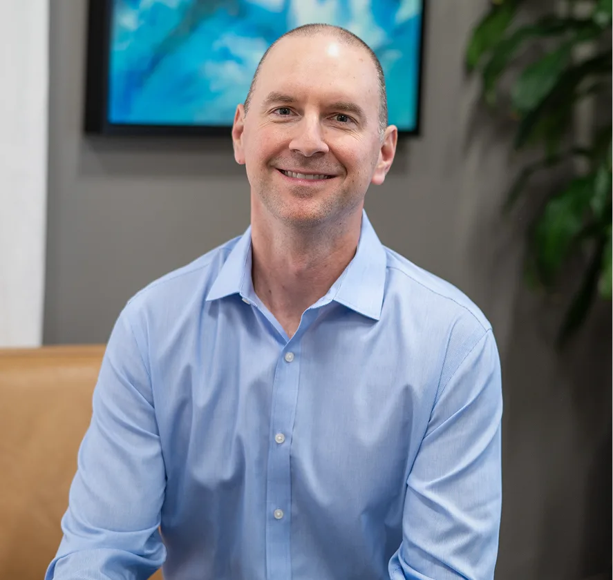 Man in light blue button-up shirt smiling in modern office setting