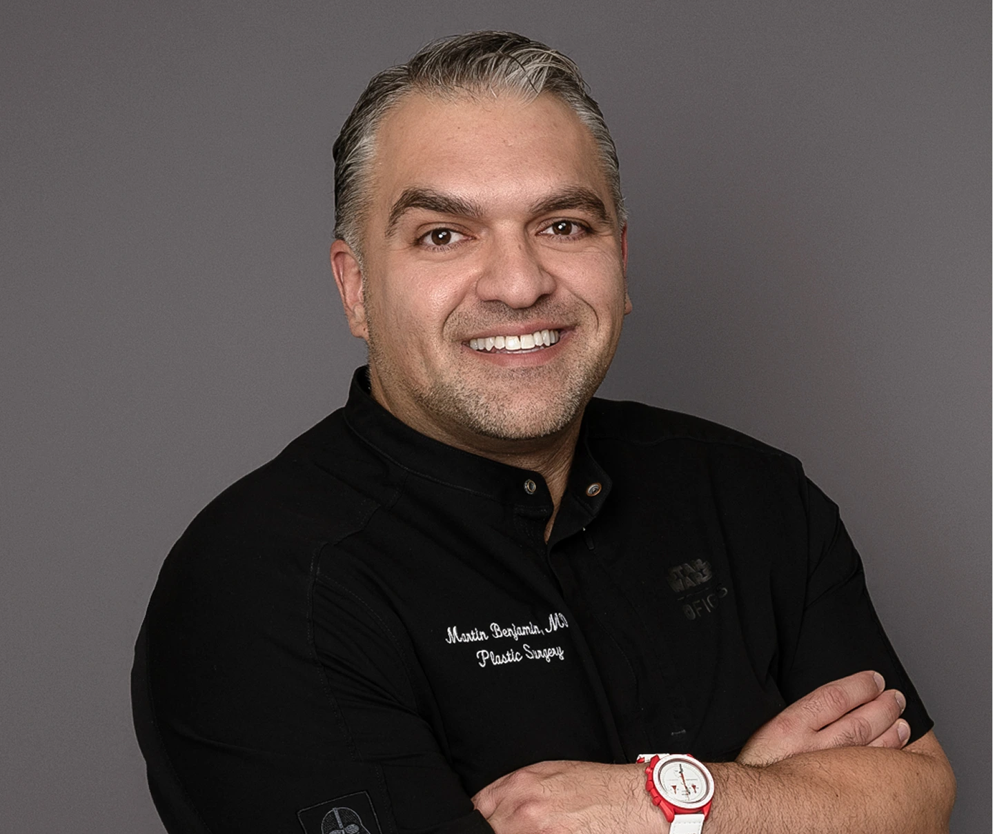Dr. Martin Benjamin, MD, plastic surgeon, smiling with arms crossed wearing black shirt