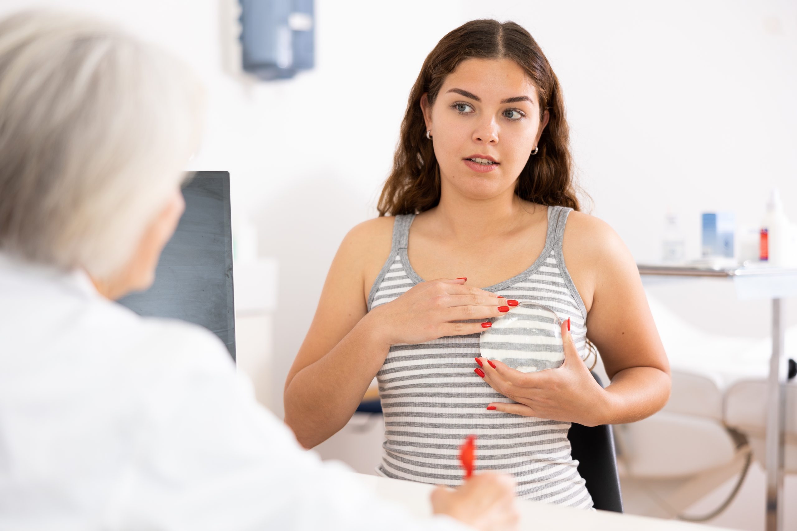 Patient in striped tank top discussing concerns with female doctor in clinical consultation room