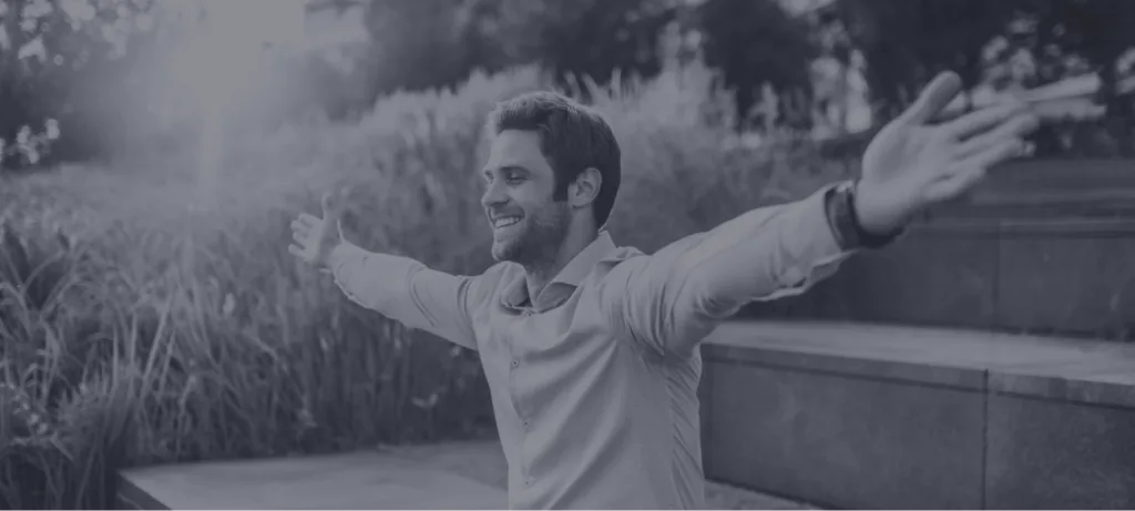 Man with arms outstretched smiling outdoors in a natural setting