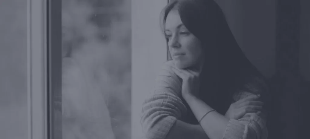 Woman looking pensively out a window with hand to face