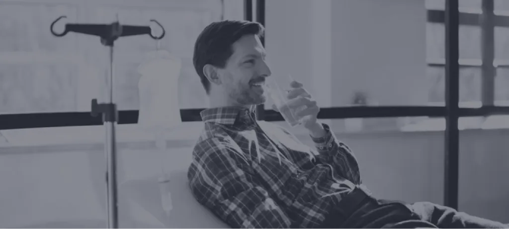 Man seated beside IV stand holding water glass during infusion treatment