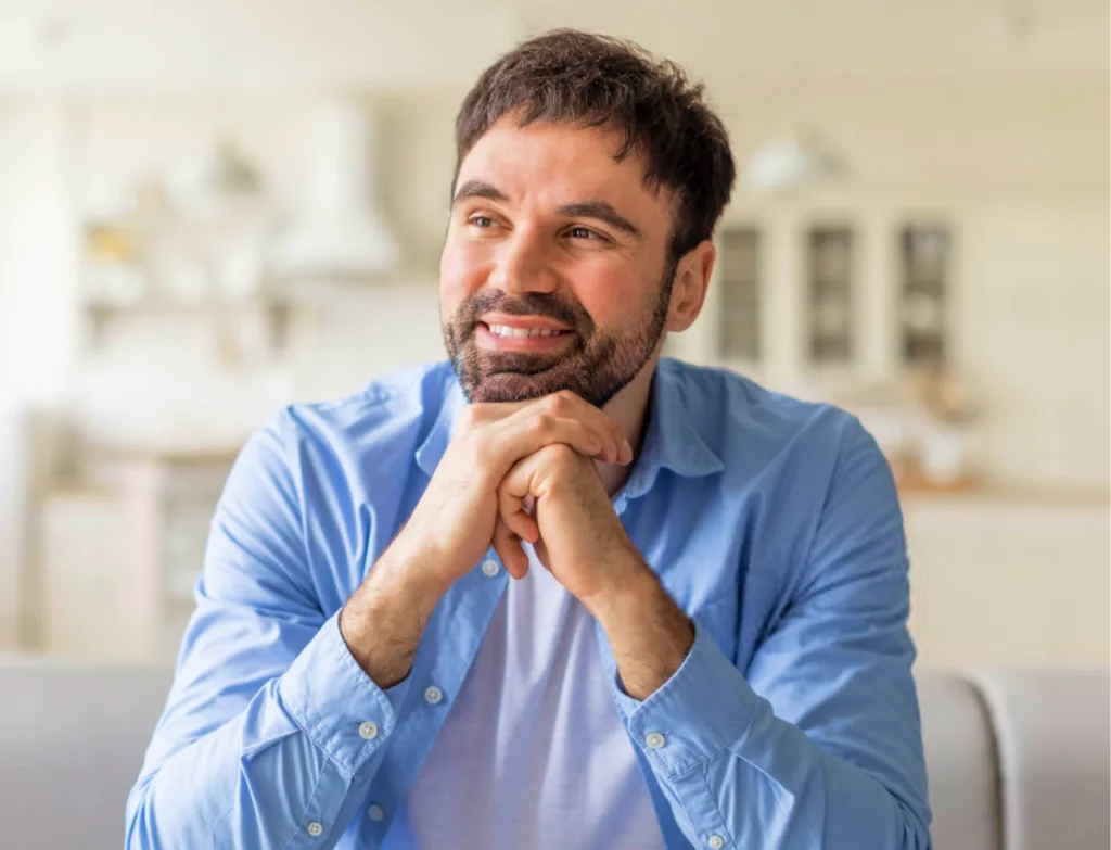 Man in blue shirt smiling with hands clasped near face in medical office setting