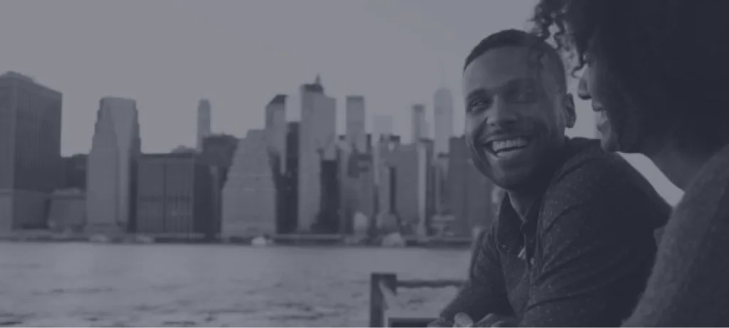 Couple smiling together with city skyline visible across water in background