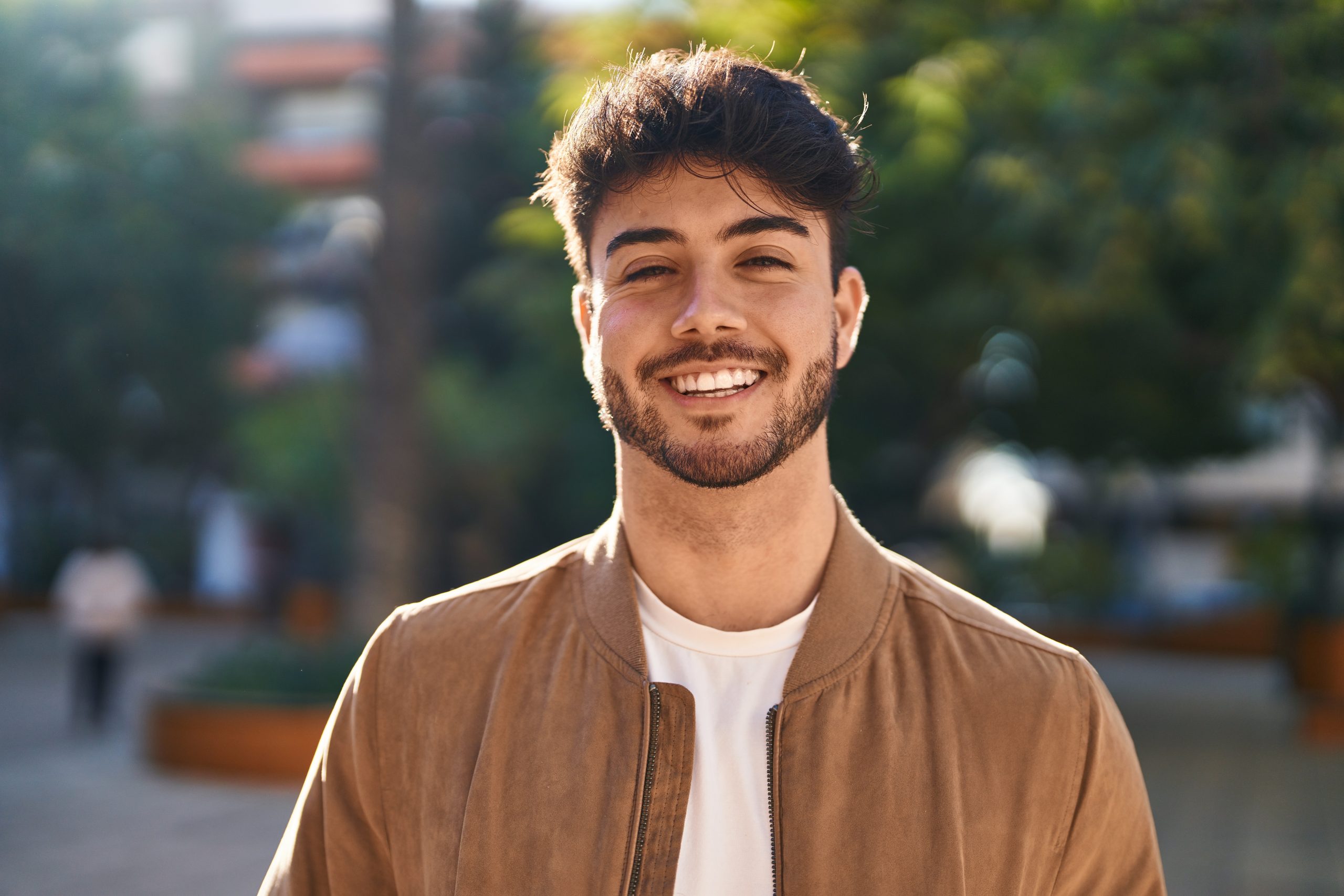 Man with beard smiling outdoors with blurred urban background