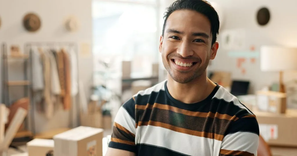 Man in striped black, orange, and white shirt smiling in modern office space