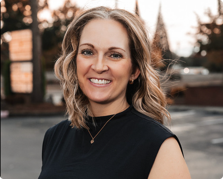 Woman with wavy shoulder-length hair smiling at camera outdoors at dusk