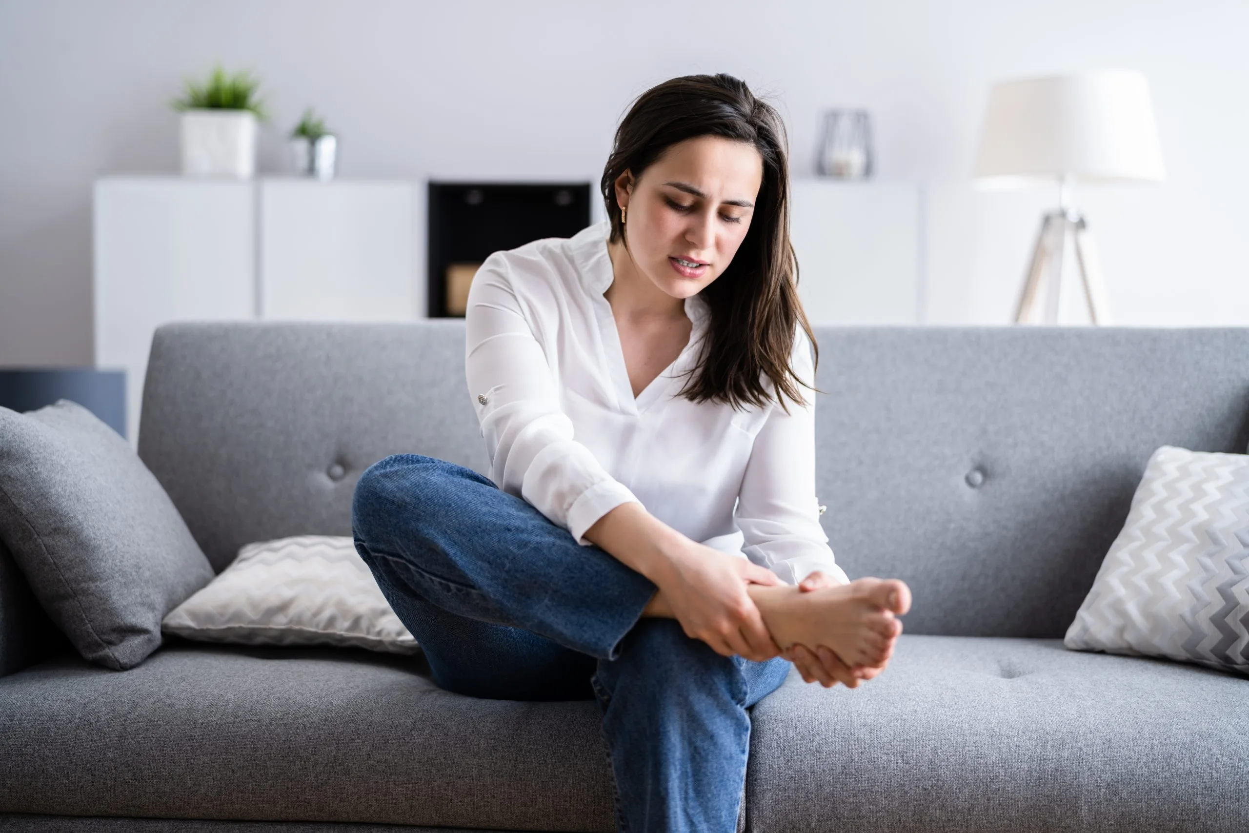 Woman sitting on a sofa holding her sore heel