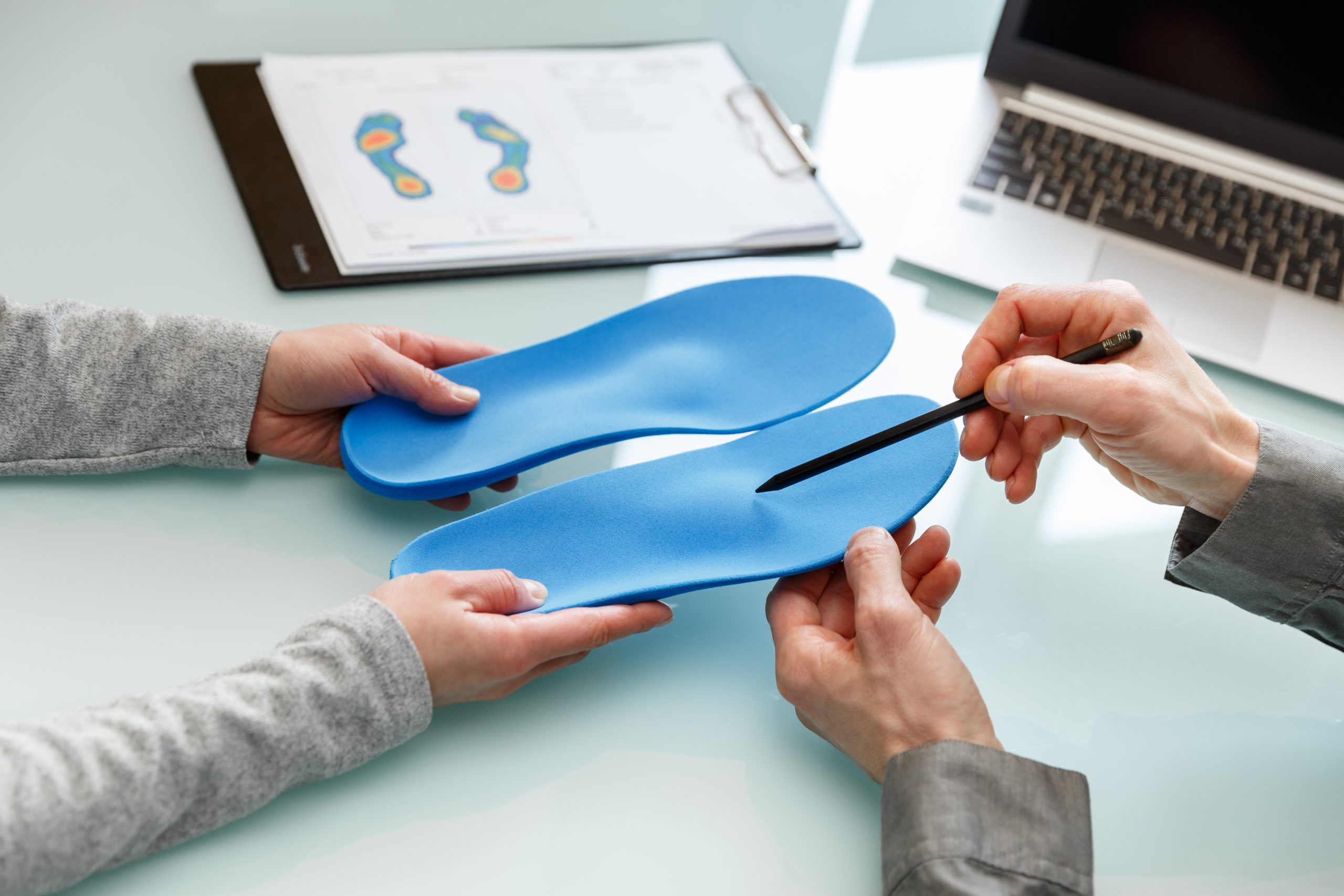 Two people examining blue orthotic shoe insoles at a desk with foot diagrams on clipboard
