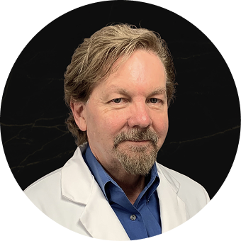 Man in white coat and blue shirt against dark background