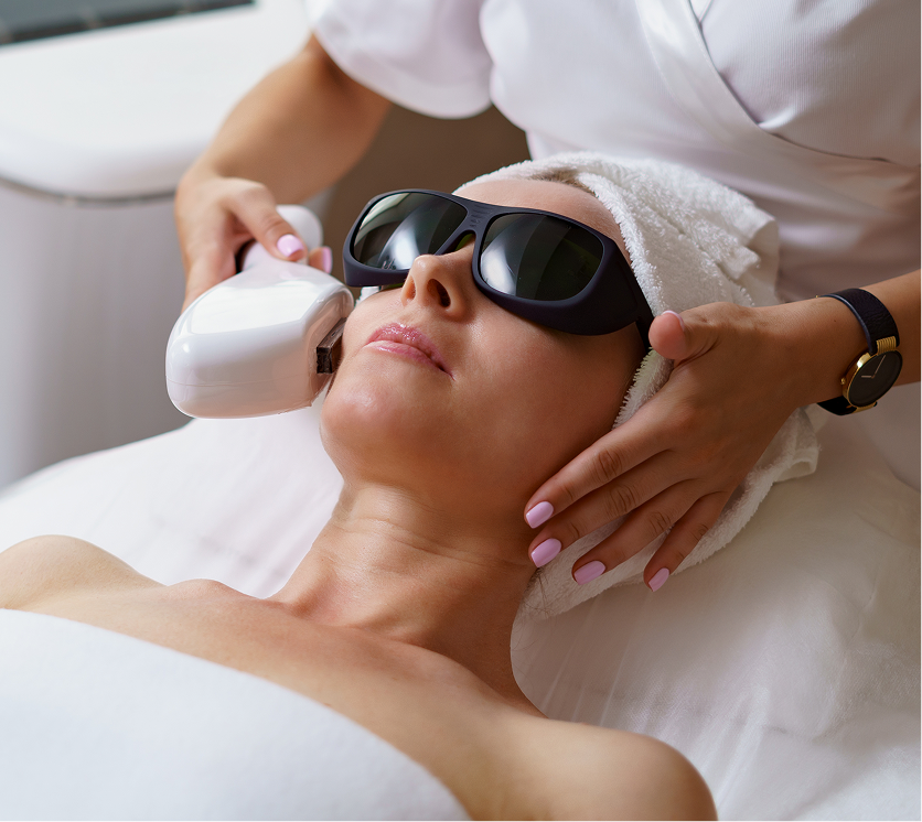 Clinician performing IPL photofacial treatment on patient's face using handheld device with protective eyewear