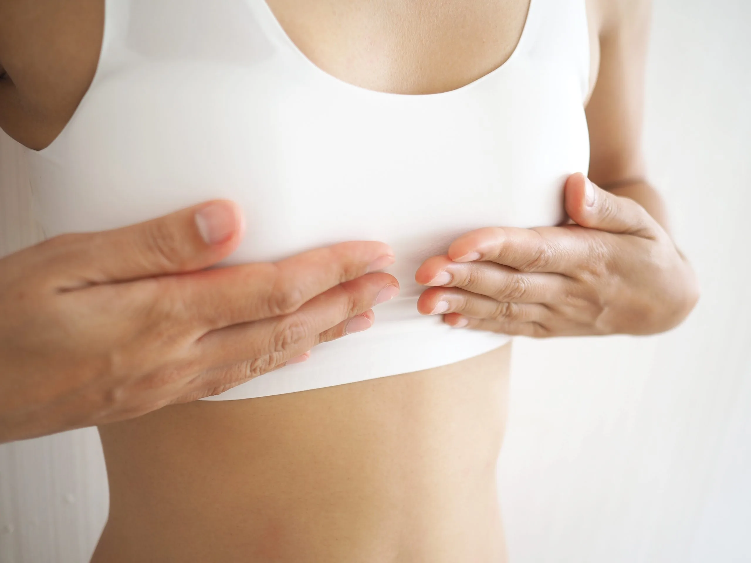 Woman in white tank top examining her chest with both hands