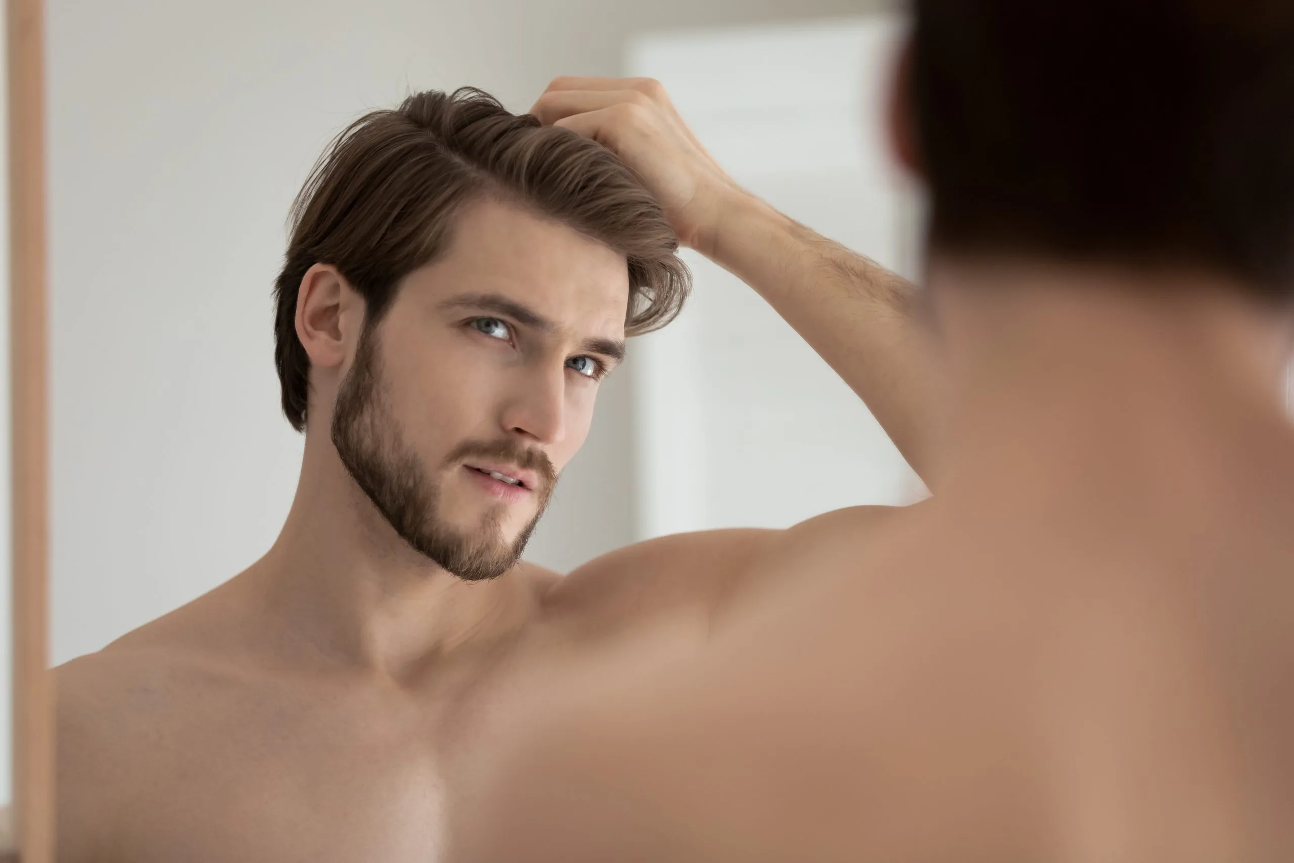 Man looking at mirror reflection while running hand through his hair