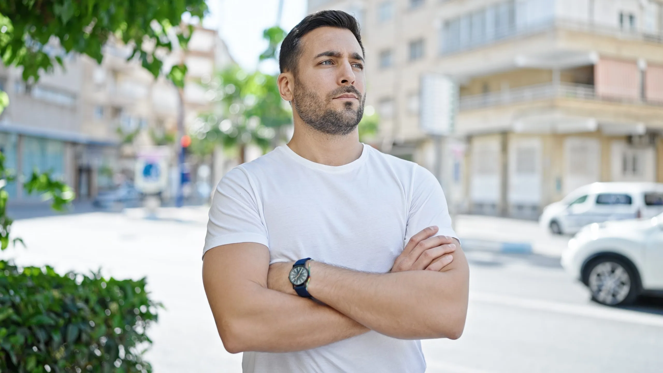 Man in white t-shirt standing with arms crossed on urban street