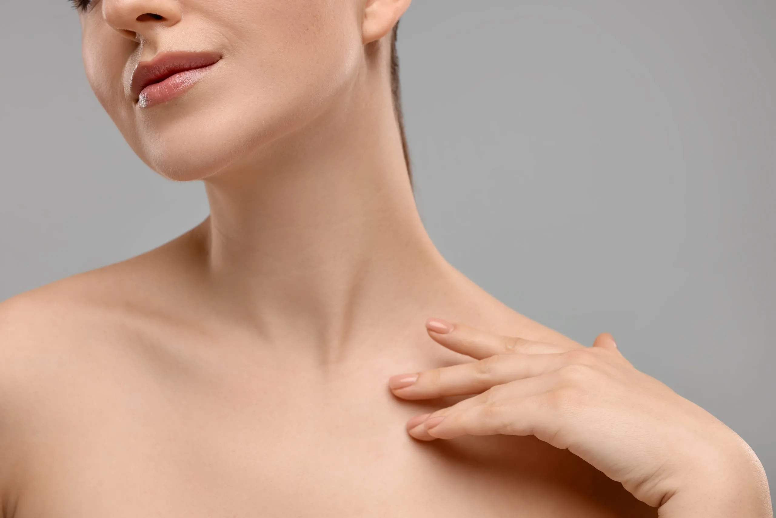 Woman touching her neck and shoulder area against gray background