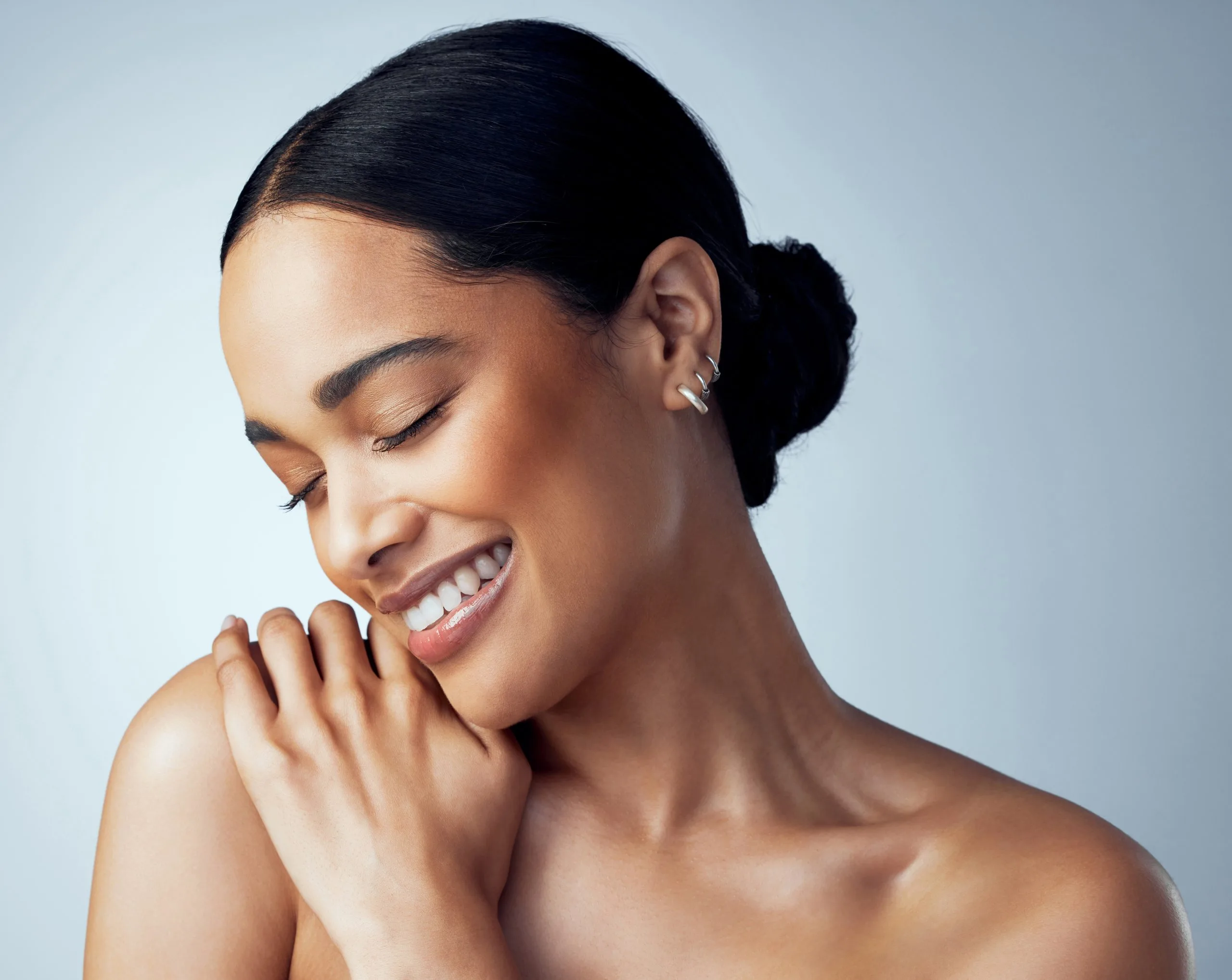 Woman touching her face with eyes closed and smiling against a light blue background