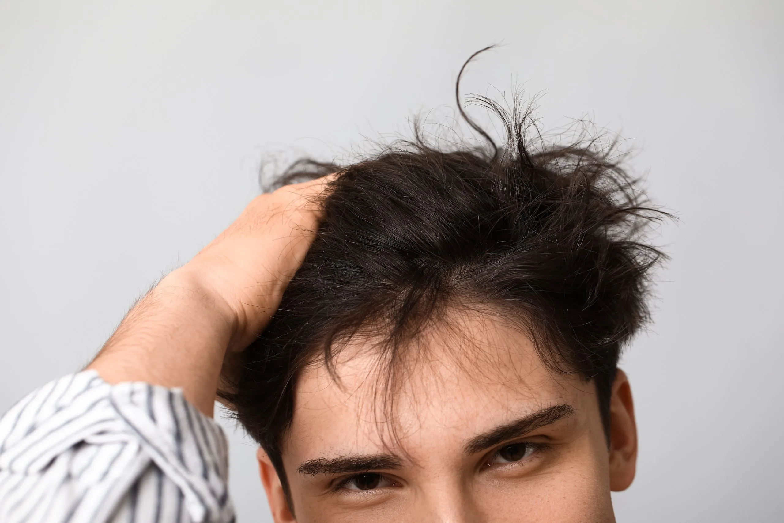 Man touching thinning hair at hairline against gray background