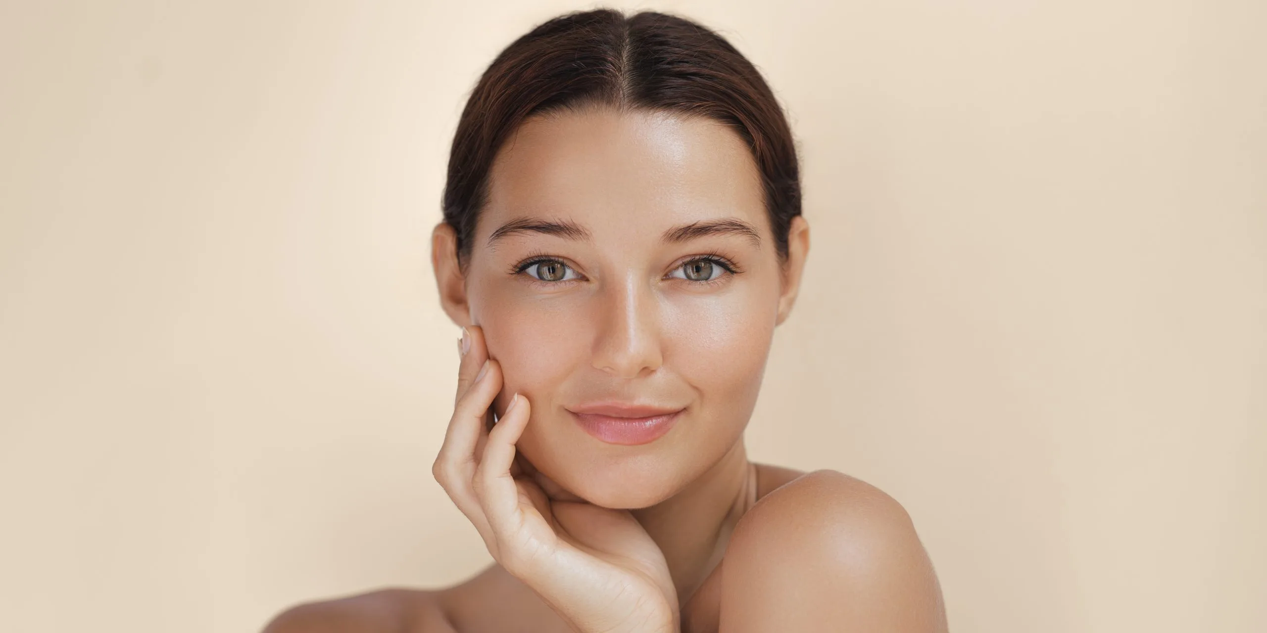 Woman with clear skin smiling at camera while touching her cheek