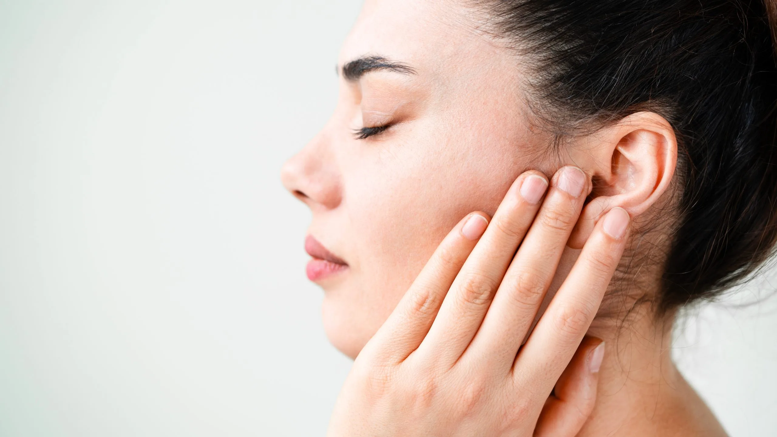 Woman in profile touching the side of her face against light background