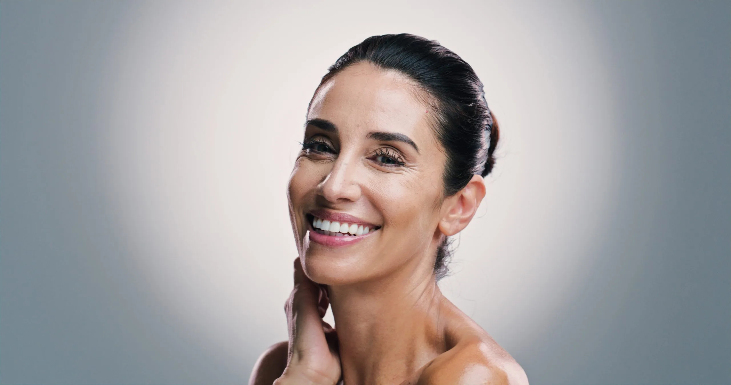 Woman with dark hair smiling at camera, hand touching her jawline